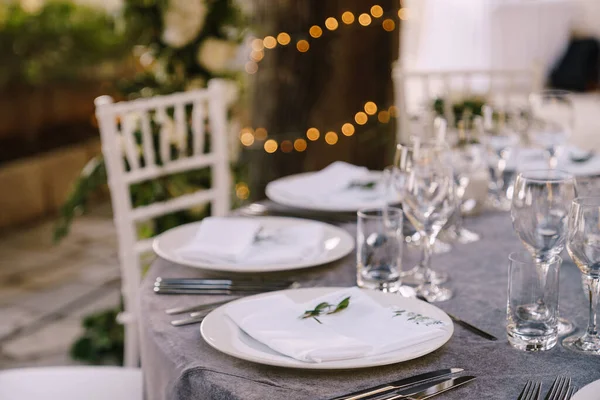 Прием свадебного ужина. Белые круглые тарелки на круглом столе с серой скатертью, белые кресла Кьявари с белыми подушками. Цветочная композиция в центре стола . — стоковое фото