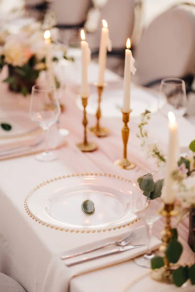 Wedding dinner table reception. Close-up of wildcard with gold beads, transparent glass. Runner of pink silk. Candles in golden candlesticks and flowers in the center of the table. — Stock Photo, Image