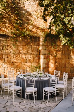 Düğün masası resepsiyonu. Gri masa örtüsü olan misafirler için yuvarlak ziyafet masaları. Çiçek aranjmanı masanın ortasına. Ağaç gövdelerinde çelenkler, havada kristal avizeler
