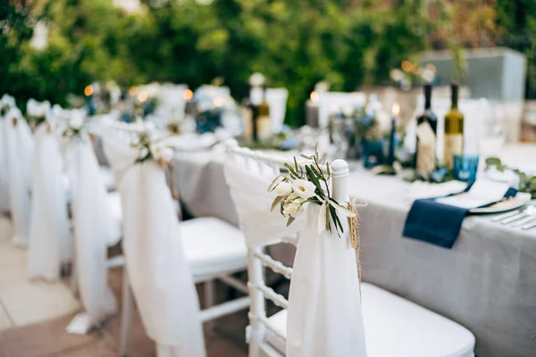 Прием свадебного ужина. Белый стул Chiavari Tiffany украшен белой тонкой тканью и цветочной композицией белых цветов, на фоне банкетного стола на свадьбе — стоковое фото