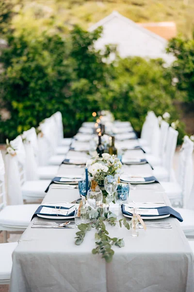 Resepsi meja makan malam pernikahan. Meja yang disajikan dengan taplak meja abu-abu dengan piring putih, dengan serbet biru. Komposisi bunga dengan eukaliptus di tengah meja. Kursi Chiavari Putih — Stok Foto