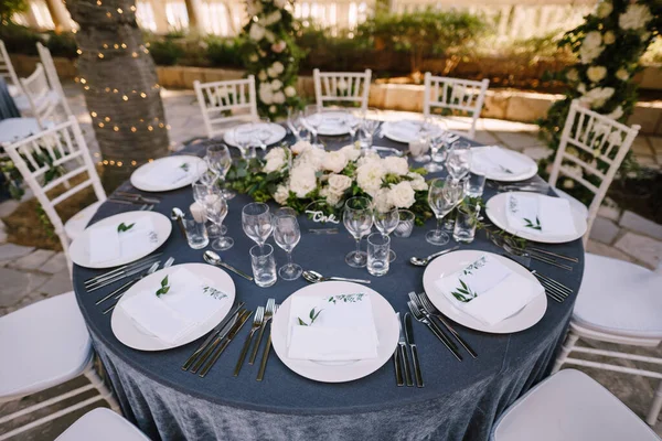 Recepción de mesa de cena de boda. Platos redondos blancos sobre una mesa redonda con mantel gris, sillas Chiavari blancas con almohadas blancas. Un arreglo floral en el centro de la mesa . — Foto de Stock