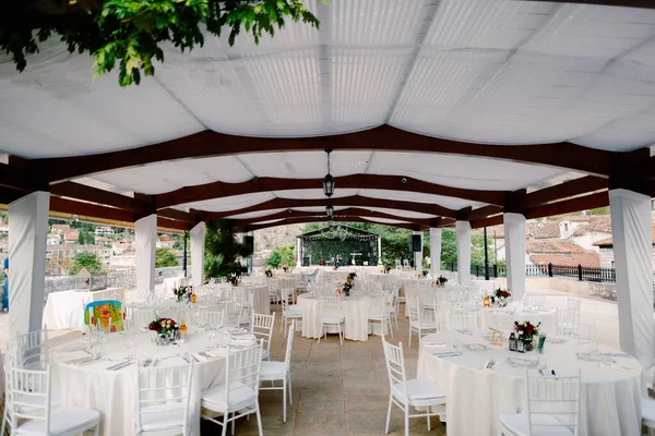 Esküvői vacsora asztal fogadás. Kerekasztal fehér abroszokkal és fehér Chiavary székekkel egy nagy fehér sátor alatt, egy zenei csoport hátterében. — Stock Fotó