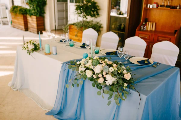 Recepción de mesa de cena de boda. Decoración de la mesa de recién casados con rosas blancas y crema, suculentas, ramas de árboles, ramas de eucalipto. Mesa rectangular con mantel blanco-azul — Foto de Stock