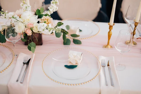 Mesa de jantar de casamento recepção. Close-up de curinga com contas de ouro, vidro transparente. Corredor de seda rosa. Velas em castiçais dourados e flores no centro da mesa . — Fotografia de Stock