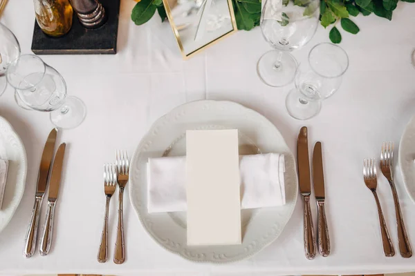 Прием свадебного ужина. Сливочный лист меню на тарелке с салфеткой из ткани. Столовые приборы выложены по правилам этикета. Вид сверху — стоковое фото