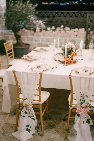 Recepción de mesa de cena de boda. Cubriendo sillas marrones Chiavari Tiffany con tela blanca al suelo, decoración con flores de rosa y peonía, sobre el fondo de una mesa cuadrada blanca con velas — Foto de Stock