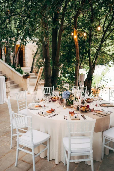 Recepción de mesa de cena de boda. Mesa redonda con mantel blanco con corredor marrón en la mesa. Viena anidada en servilletas marrones, un ramo de flores está sobre la mesa. Sillas Chiavari blancas con almohadas . — Foto de Stock