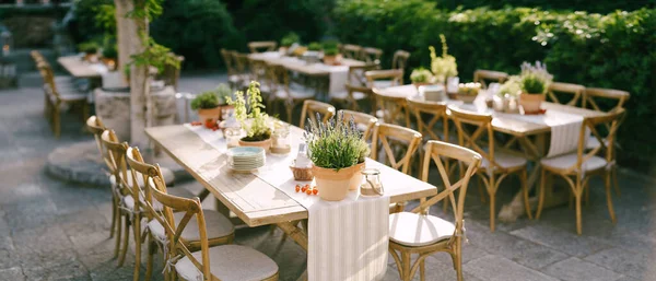 Table de mariage réception au coucher du soleil à l'extérieur. Anciennes tables rectangulaires en bois avec chemin de chiffon, chaises vintage en bois, pots de lavande, tomates cerises et pots en argile avec citrons sur les tables — Photo