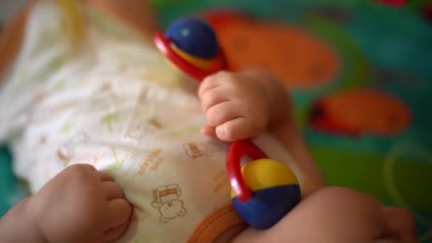 Il bambino giace sulla schiena sul tappeto di sviluppo e gioca con il sonaglio — Video Stock