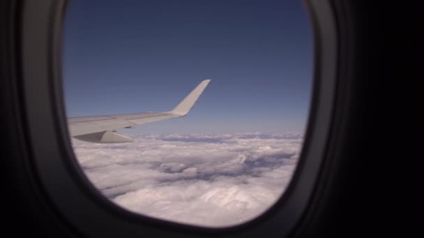 Blick aus dem Bullauge des Passagierflugzeugs. Das Flugzeug fliegt über dicke Wolken, die Kamera zeigt den Flügel, Das Konzept des Reisens und ein reiches Leben — Stockvideo