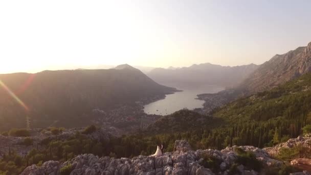 The bride and groom stand at top of Mount Lovchen in Montenegro with fantastic view of Kotor Bay, Kotor old town, Prcanj, Muo, to the tops of mountains and forests, flooded with sunset sunshine — Stock Video