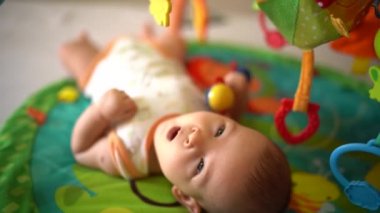 Bebek renkli minderde oynuyordu. Minder üzerinde oyuncak ile oynayan sevimli erkek bebeğe yakın çekim. Çıngırakla sevimli çocuk oyunu. Çocuk eğlencesi etkinliği