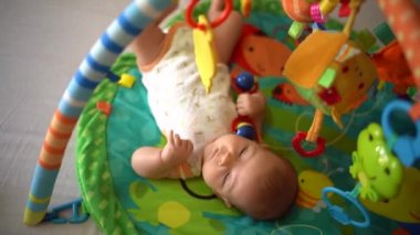 Bebek, elinde çıngıraklı bir çıngırakla gelişim minderinde oyuncaklarla oynanıyor. Renkli bir mindere uzanmış sevimli bir bebek. Yenidoğan 'ın Aile ve Gelişim Konsepti