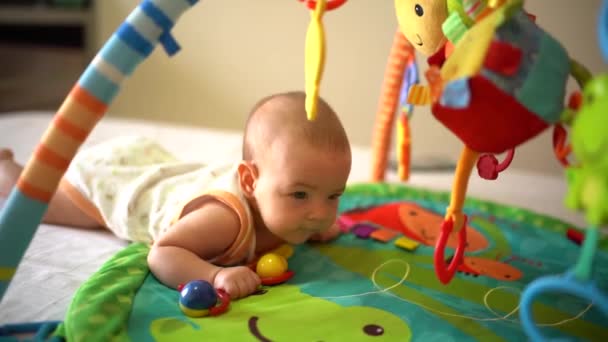 Bambino con sonaglio in mano, cercando di strisciare sul tappeto di sviluppo del gioco — Video Stock