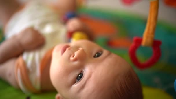 귀여운 아기가 장난감 놀이를 한다. 화려 한 매트 위에 누워 있는 귀여운 남자 아이를 클로즈업합니다. 사랑 스러운 아기의 모습. 행복 한 유아 연구 세계 — 비디오