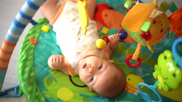 Söt bebis som leker leksak. Närbild av söt liten pojke som ligger på färgglada matta. Porträtt av en bedårande bebis. Glad barndoms studievärld — Stockvideo
