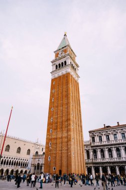 Piazza San Marco 'daki kırmızı tuğladan yapılmış dev çan kulesi Venedik, İtalya' daki St. Marks Katedrali 'nin Campanile' i. Meydandaki kulenin eteklerinde turist kalabalığı var.