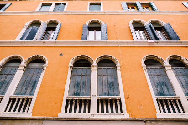 Vysoká oblouková okna v oranžové budově v Benátkách v Itálii. Modré dřevěné okenice na starých dřevěných oknech. — Stock fotografie