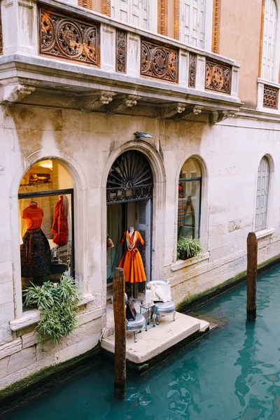 意大利威尼斯- 2019年10月4日：意大利威尼斯时装店展示。花哨的橙色衣服60-70年代在一个模特身上。蓝色水中储存的门槛. — 图库照片