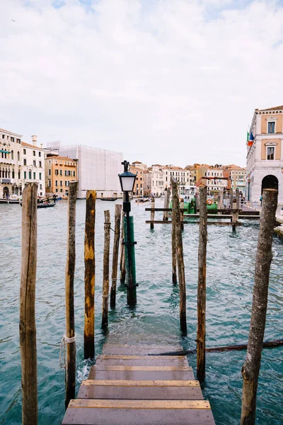 Muelle de madera para barcos y góndolas en Italia, en Venecia. Una escalera de madera va bajo el agua, montones verticales de troncos de árboles. Gran canal con agua de mar de color azul . — Foto de Stock