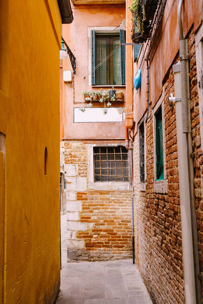 Close-ups of building facades in Venice, Italy. Cozy Venetian streets. Narrow street, between two houses. The first floor is a bare red brick, second floor is a pink painted wall.