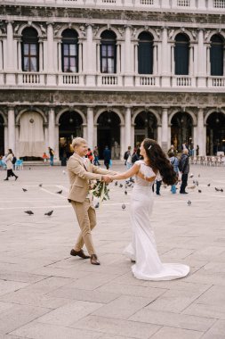 Düğün Venedik, İtalya 'da. Gelin ve damat, San Marco Meydanı 'ndaki güvercinlerin arasında Venedik Ulusal Arkeoloji Müzesi' nin arka planında dans ediyorlar..