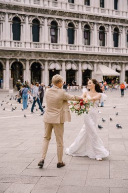 Düğün Venedik, İtalya 'da. Gelin ve damat, San Marco Meydanı 'ndaki güvercinlerin arasında Venedik Ulusal Arkeoloji Müzesi' nin arka planında dans ediyorlar..