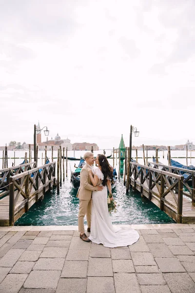 Bruidegom en staan naast de gondelpier, knuffelen, in Venetië, in de buurt van Piazza San Marco, met uitzicht op San Giorgio Maggiore en de zonsondergang hemel. De grootste gondelpier van Venetië, Italië. — Stockfoto