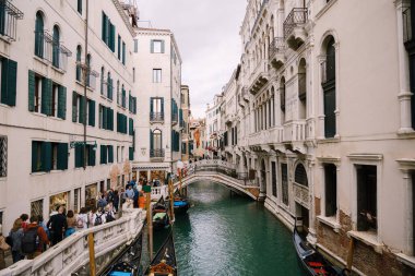 Venedik, İtalya - 04 Ekim 2019: İtalya 'da Venedik sokaklarında binalar arasında dar bir kanal yakınında bir turist topluluğu yürüyor. Deniz suyu üzerinde küçük kemerli köprüler.