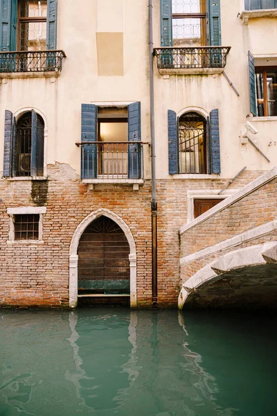 Цегляний будинок у воді в Італії, Венеція. Цегляний міст через невеликий вузький канал, класичні венеціанські вікна на фасаді будівлі з дерев'яними віконцями і ковані бруси.. — стокове фото
