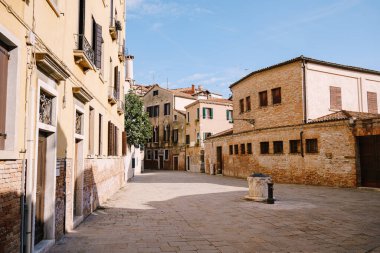 Terk edilmiş bir Venedik sokağı gün batımı ışığıyla doldu. İtalya 'da Venedik meydanının ortasında metal bir kolona sahip antik bir taş kuyusu.