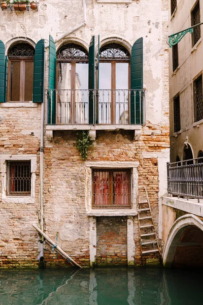 Будівництво фасадів у Венеції, Італія. Прекрасні венеціанські вікна з відкритими дерев'яними віконцями. Старий будинок з червоної цегли поруч з мостом через вузький канал.. — стокове фото