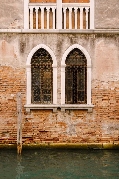 La fachada de un edificio corporativo de apartamentos en Venecia, Italia. Edificios en aguas del Canal Veneciano. Típicas ventanas venecianas con arcos, columnas y una parte superior afilada, en la pared de una casa de piedra . — Foto de Stock