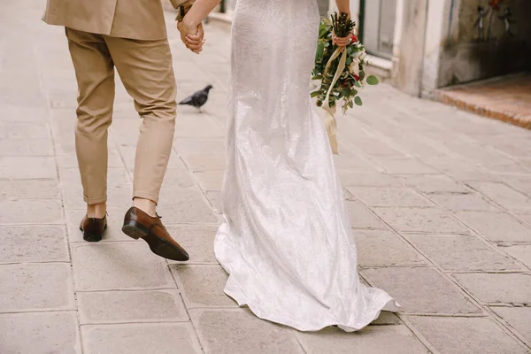 Italy wedding in Venice. The bride and groom walk along the deserted streets of the city. Closeup of the legs of the newlyweds and a long train of the brides dress. — Stock Photo, Image