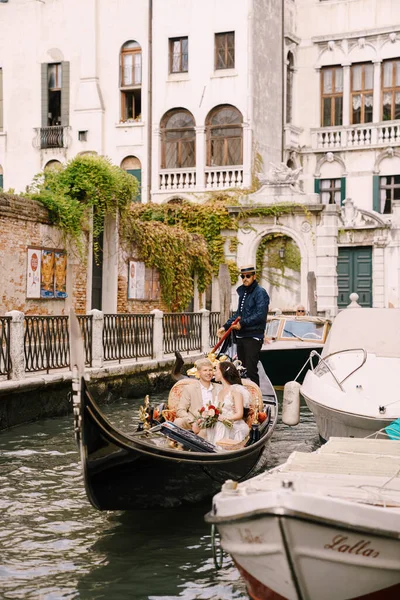 Venecia, Italia - 04 de octubre de 2019: Italia boda en Venecia. Un gondolero enrolla a los novios en una clásica góndola de madera a lo largo de un estrecho canal veneciano. Los recién casados están sentados en un barco — Foto de Stock