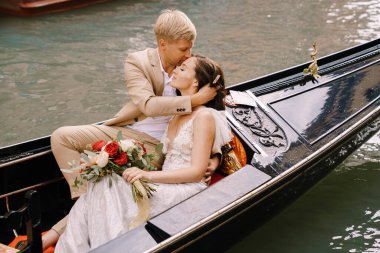 İtalya düğünü Venedik 'te. Gelin ve damat, dar bir Venedik kanalı boyunca klasik bir ahşap gondola biniyor. Kucaklaşan yeni evlilere yakın çekim.