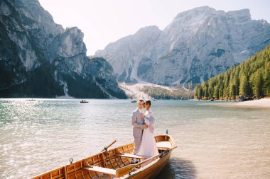 Gelin ve damat, İtalya 'daki Lago di Braies gölünde kürekleriyle ahşap bir teknede yelken açıyorlar. Avrupa 'da düğün - Yeni evliler bir teknede birbirlerine sarılıyorlar.