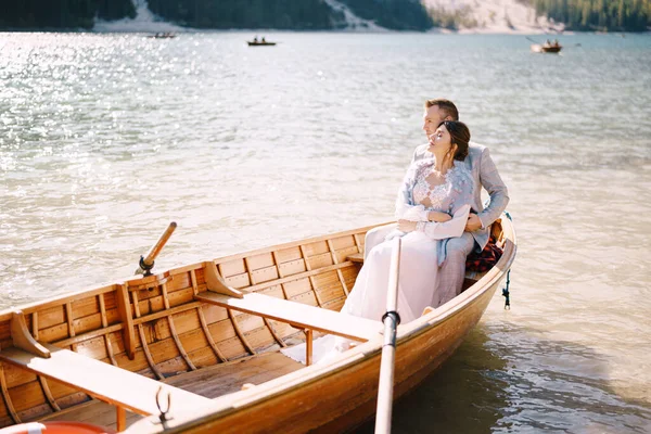 Een bruidspaar zit in een houten boot op het Lago di Braies in Italië. Pasgetrouwden in Europa, op Braies Lake, in de Dolomieten. De bruidegom knuffelt de bruid. — Stockfoto
