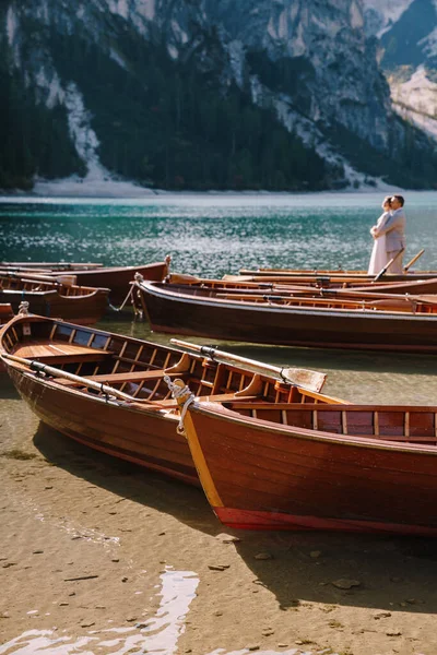 Novia y novio navegando en barco de madera, con remos en Lago di Braies lago en Italia. Boda en Europa - Recién casados están de pie abrazando en un barco . — Foto de Stock