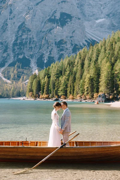 Bruid en bruidegom in een houten boot bij het Lago di Braies in Italië. Bruidspaar in Europa, aan het Braies meer, in de Dolomieten. De pasgetrouwden staan in de boot en knuffelen. — Stockfoto