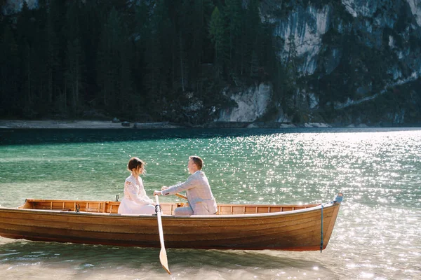 A friss házasok egy fából készült hajóval hajóznak a Lago di Braies-en Olaszországban. Esküvő Európában, a Braies tónál. Esküvői pár - A vőlegény evezős sorok, a menyasszony szemben ül. — Stock Fotó