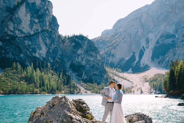 Les mariés se tiennent debout sur des pierres surplombant le lac de Braies en Italie. Mariage de destination en Europe, sur le lac de Braies. Aimer les jeunes mariés marcher dans le contexte de la nature étonnante . — Photo