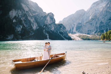 Gelin ve damat, İtalya 'daki Lago di Braies gölünde kürekleriyle ahşap bir teknede yelken açıyorlar. Avrupa 'da düğün - Yeni evliler bir teknede birbirlerine sarılıyorlar.