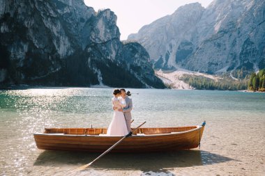 Gelin ve damat, İtalya 'daki Lago di Braies gölünde kürekleriyle ahşap bir teknede yelken açıyorlar. Avrupa 'da düğün - Yeni evliler bir teknede birbirlerine sarılıyorlar.