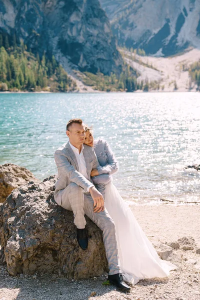 Жених и невеста сидят на фоне камней на Лаго-ди-Брайс в Италии. Свадьба в Европе, на озере Брэйс. Любящие молодожены ходят на фоне удивительной природы — стоковое фото