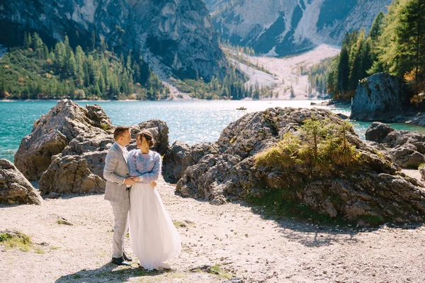 Noiva e noivo estão contra o pano de fundo de pedras com vista para Lago di Braies, na Itália. Casamento de destino na Europa, no lago Braies. Amantes recém-casados caminhar contra o pano de fundo de natureza incrível . — Fotografia de Stock