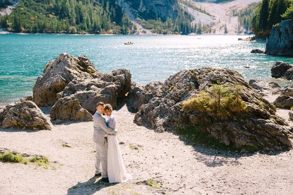 Νύφη και γαμπρός σταθεί στο φόντο των λίθων με θέα Lago di Braies στην Ιταλία. Γάμος στην Ευρώπη, στη λίμνη Μπρέις. Οι ερωτευμένοι νεόνυμφοι περπατούν στο φόντο της εκπληκτικής φύσης. — Φωτογραφία Αρχείου