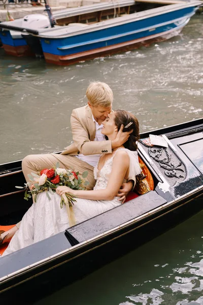 Italië bruiloft in Venetië. De bruid en bruidegom rijden in een klassieke houten gondel langs een smal Venetiaans kanaal. Close-up van knuffels pasgetrouwden. — Stockfoto