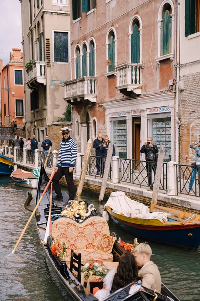Венеція, Італія - 04 жовтня 2019: Італійське весілля у Венеції. Гондольєр кидає наречену з нареченим у класичну дерев'яну гондолу по вузькому венеціанському каналу. Молоді сидять у човні і цілуються.. — стокове фото